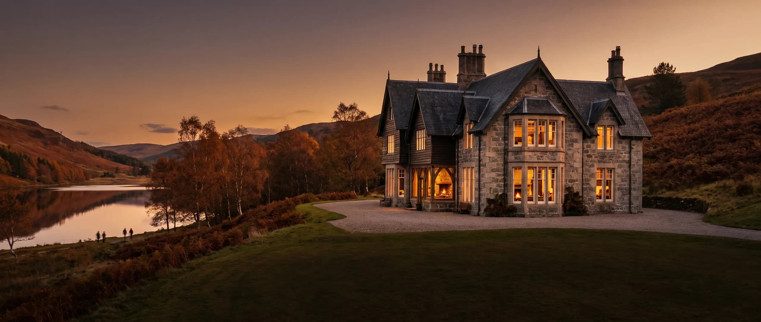 The granite and timber lodge at golden hour, lit windows above a lawn, the loch and bracken hills beyond